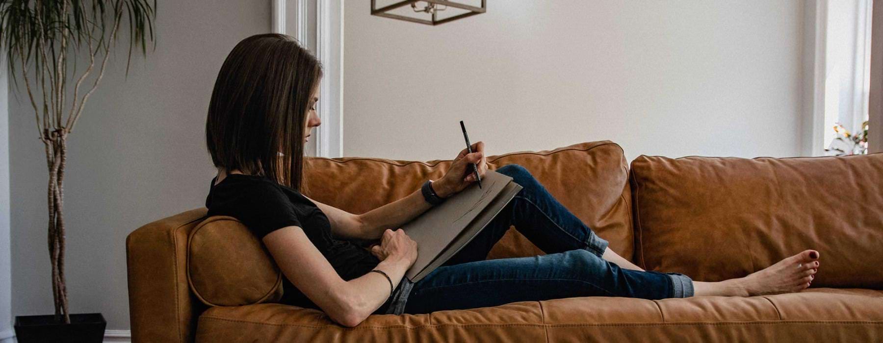 woman lies on a couch and draws on a large sketch pad